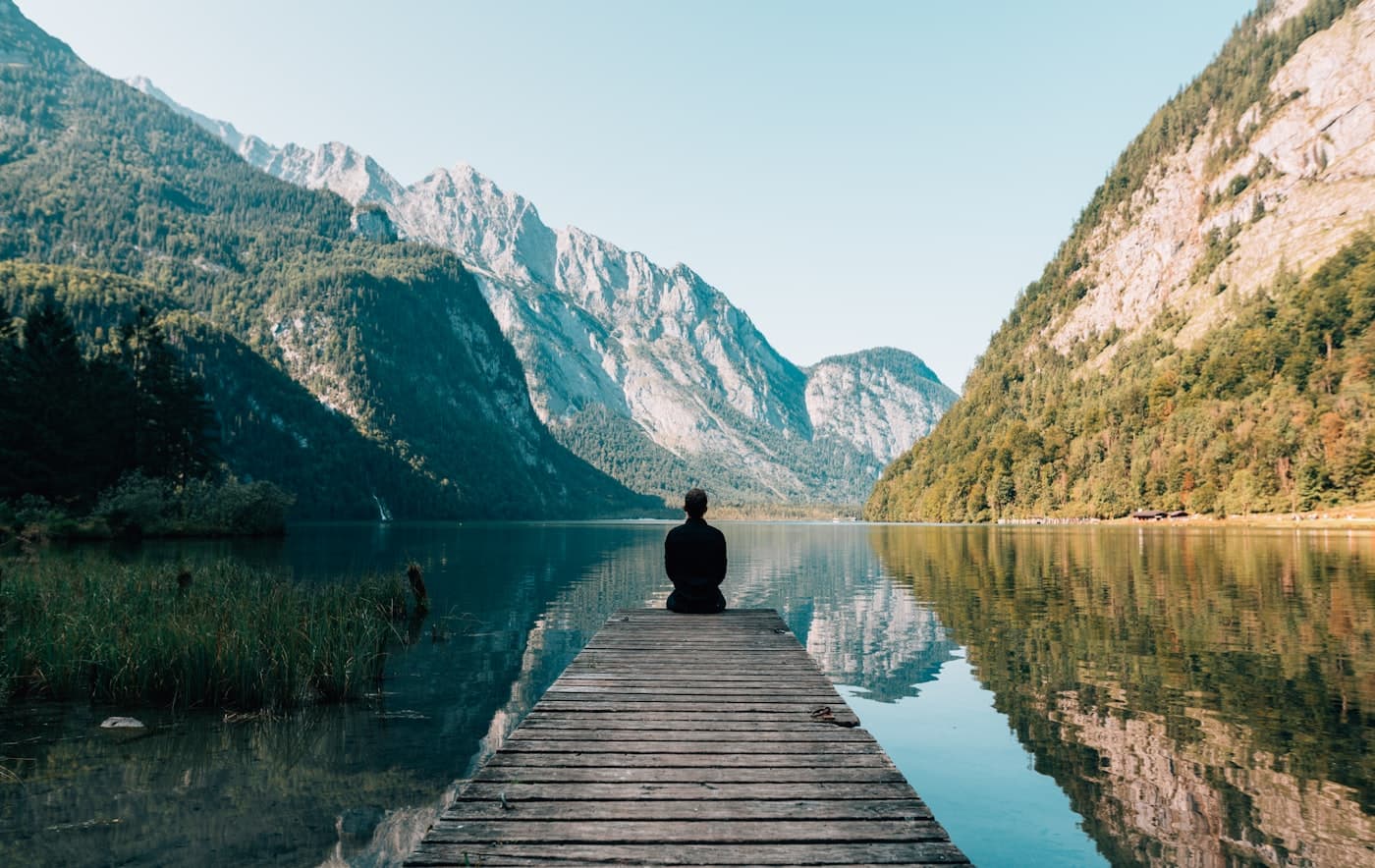 Traveller seated at the end of a mountain lake dock